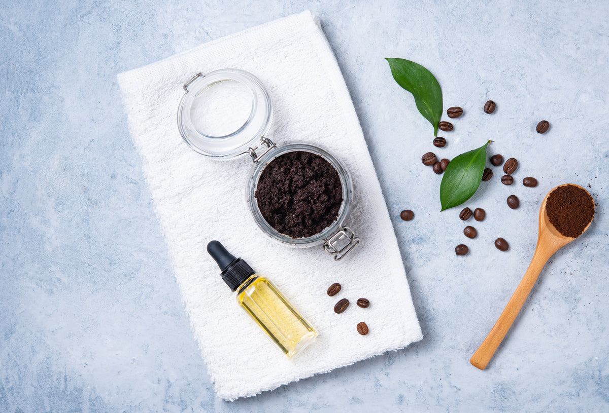 Kaffeepeeling im Glas, Pflegeöl und Kaffeebohnen auf einem weißen Handtuch